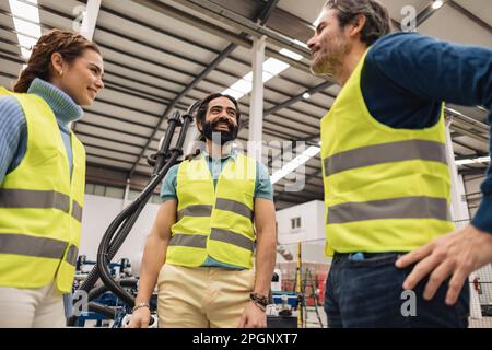 Happy engineers wearing reflective clothing talking with each other in factory Stock Photo