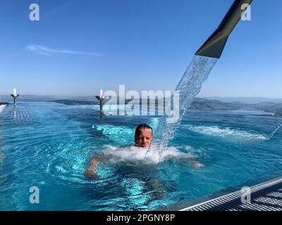 Man Enjoy Infinity Swimming Pool with Mountain and Lake Lucerne View in a Sunny Day in Burgenstock, Nidwalden, Switzerland. Stock Photo