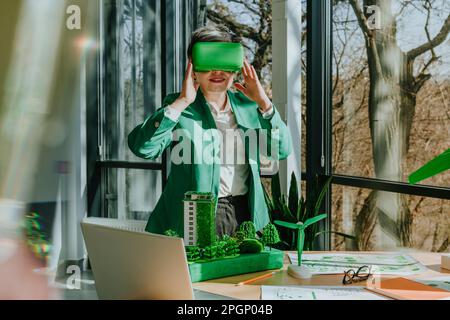 Mature businesswoman wearing VR glasses standing in green office Stock Photo