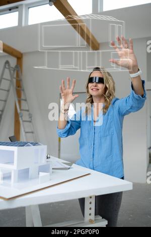 Smiling architect wearing virtual reality simulator examining house model over table Stock Photo