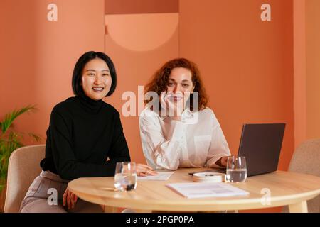 Smiling multiracial colleagues sitting at desk with laptop in office Stock Photo