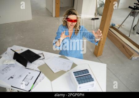 Architect wearing virtual reality simulator gesturing and examining house model Stock Photo