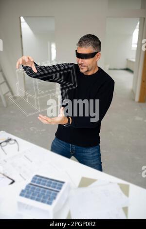 Mature architect wearing virtual reality simulator examining model home at construction site Stock Photo