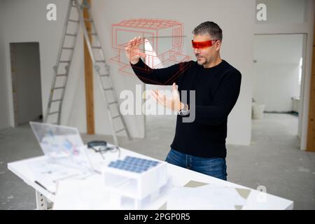 Architect wearing virtual reality simulator examining house model and gesturing at construction site Stock Photo