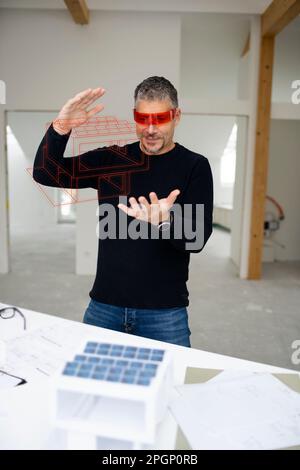Architect wearing virtual reality simulator examining model home at construction site Stock Photo