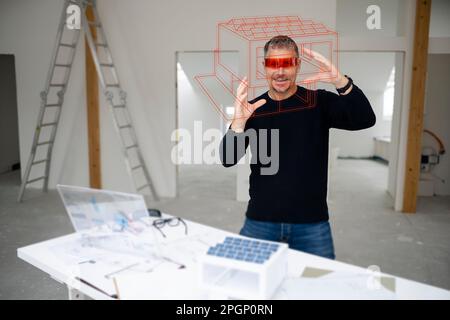 Smiling mature architect wearing virtual reality simulator examining house model at construction site Stock Photo