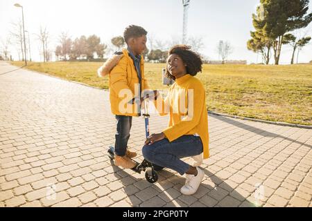 Boy on push scooter with mother on footpath in park Stock Photo