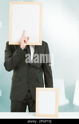 Sign-headed man framed in an office, he is standing with his finger in front of his face making the gesture of silence. On the desk in front of him is Stock Photo