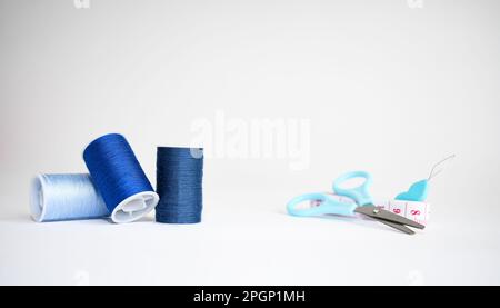 Sewing kit consisting of three spools of blue thread in different shades, scissors and measuring tape on a white background. Copy space Stock Photo