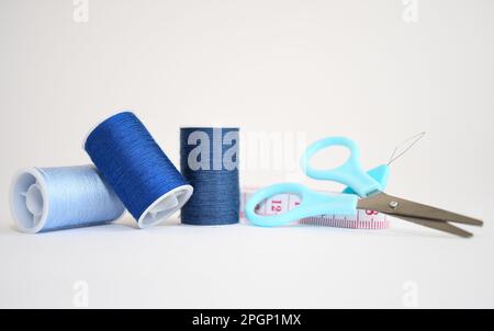 Sewing kit consisting of three spools of blue thread in different shades, scissors and measuring tape on a white background. Copy space Stock Photo