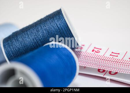 take about two spools of blue thread of different shades and a white tape measure with red numbers on a white background. Stock Photo