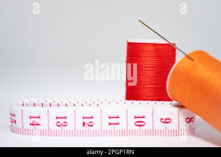 take about two spools of orange thread of different shades, a needle and a white measuring tape with red numbers on a white background. Copy space Stock Photo
