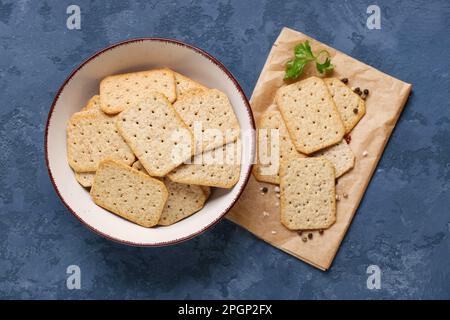 Bowl and parchment with tasty crackers on blue background Stock Photo