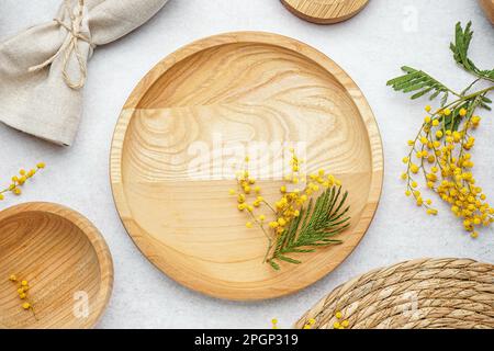 Composition with clean wooden dishes, napkin and mimosa flowers on white grunge table Stock Photo