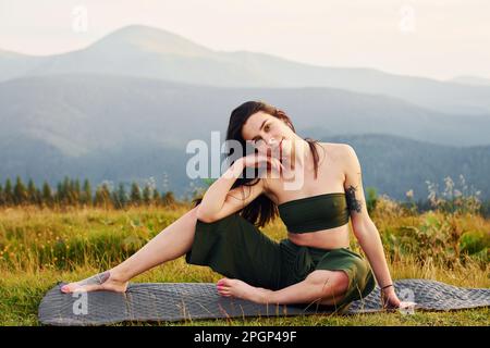 Cute brunette sits on yoga mat. Majestic Carpathian Mountains