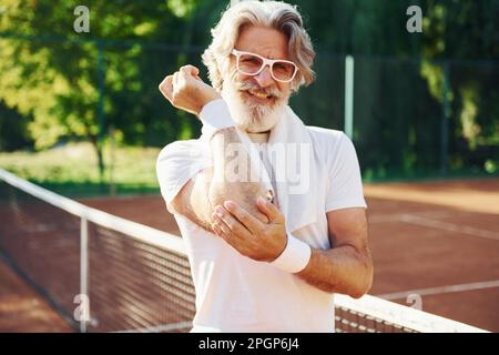 Feeling pain because of trauma. Senior modern stylish man outdoors on the sportive field at daytime Stock Photo