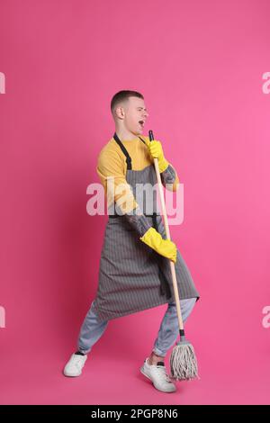 Handsome young man with mop singing on pink background Stock Photo