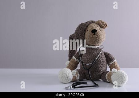 Toy bear with stethoscope on white table against light grey background, space for text. Children's hospital Stock Photo