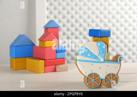 Tasty cookie in shape of stroller and colorful cubes on white wooden table, space for text. Baby shower party Stock Photo