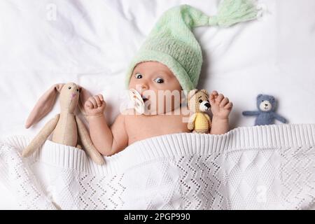 Cute little baby with toys lying under knitted plaid in bed, top view Stock Photo
