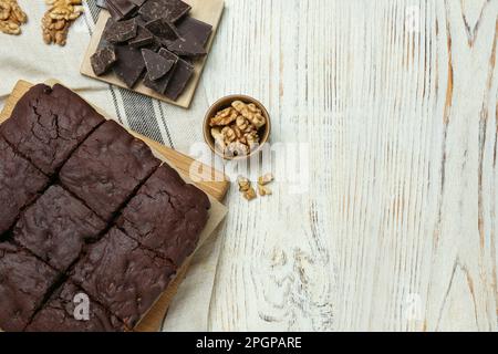 Delicious freshly baked brownies, walnuts and pieces of chocolate on white wooden table, flat lay. Space for text Stock Photo