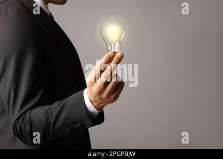 Glow up your ideas. Closeup view of businessman holding light bulb on grey background, space for text Stock Photo
