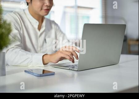 Cropped image of a handsome millennial Asian businessman or male office worker using his laptop computer at his desk. typing on keyboard, browsing int Stock Photo
