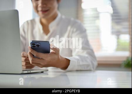 Close-up image of a happy millennial Asian businessman or male office worker using his phone at her office desk. Stock Photo