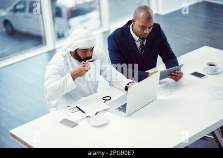 It takes two to tackle this project. two businessmen using a digital tablet and laptop while having a discussion in a modern office. Stock Photo