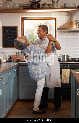 Do more things that make each other happy. a happy mature couple dancing together while cooking in the kitchen at home. Stock Photo
