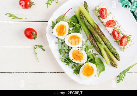 Green asparagus with boiled eggs and sandwich cream cheese on a white plate. Top view, flat lay Stock Photo