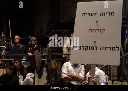 A right wing counter protester holds up a sign which reads 'A Jewish state precedes a democratic state' as anti-government protesters demonstrate against PM Benjamin Netanyahu's right-wing coalition and its proposed judicial changes near his private home on March 23, 2023 in Jerusalem, Israel. Stock Photo