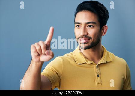 Pointing, finger and asian man with invisible hologram in studio with mockup against blue background. Interface, hand and creative male entrepreneur Stock Photo