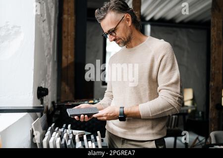 White middle-aged male interior designer in eyeglasses working with samples in workshop Stock Photo