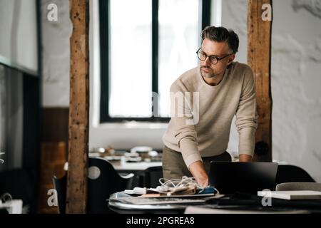 Pensive white middle-aged man in eyeglasses working with laptop in office Stock Photo