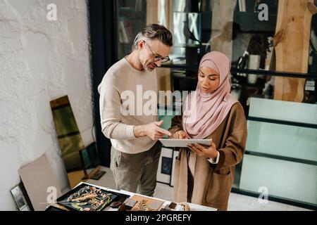 Two multiracial colleagues designers using tablet while working together in modern office Stock Photo