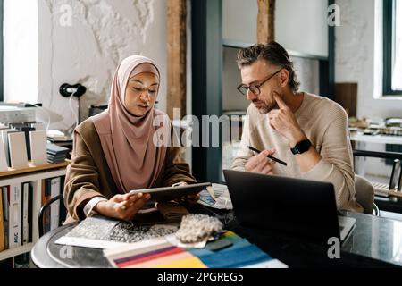 Two multinational colleagues designers working with laptop computer at workshop indoors Stock Photo