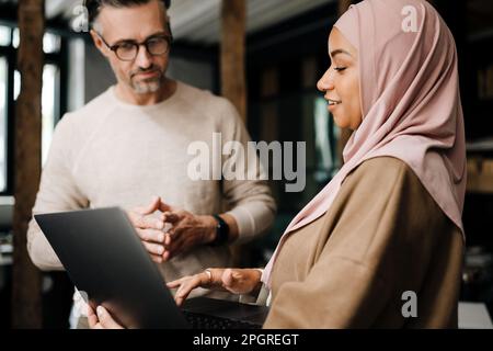 Two multinational colleagues working with laptop computer in modern office Stock Photo