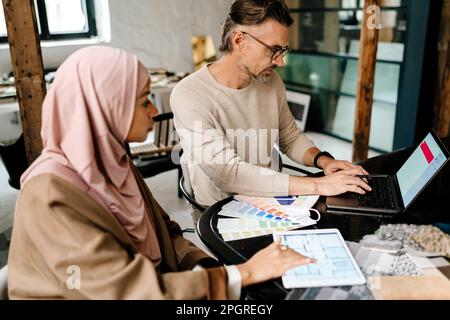Two multinational colleagues designers working with computers together sitting at table in office Stock Photo