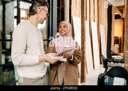 Two cheerful multiracial colleagues designers using tablet while working together in modern office Stock Photo