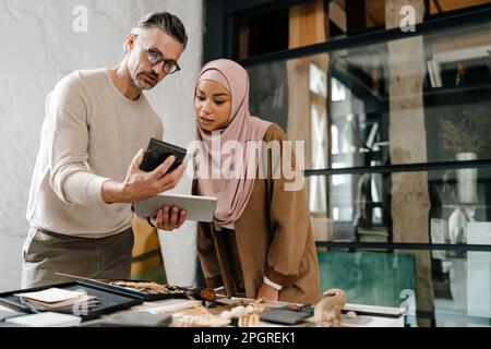 Two multiracial colleagues designers using tablet while working together in modern office Stock Photo