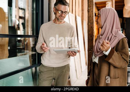 Two cheerful multiracial colleagues using tablet while working together in modern office Stock Photo