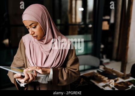 Arabian woman wearing hijab working on tablet computer while standing in modern office Stock Photo