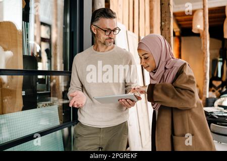 Two cheerful multiracial colleagues using tablet while working together in modern office Stock Photo