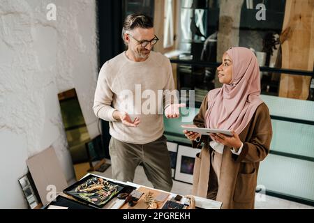 Two multiracial colleagues designers using tablet computer while working together in workshop Stock Photo