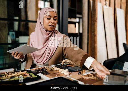 Female muslim architect wearing headscarf working on tablet in modern office Stock Photo