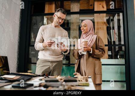 Two multiracial colleagues designers using tablet computer while working together in workshop Stock Photo