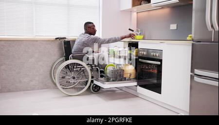 Young Man Sitting On Wheelchair Arranging Plates In Dishwasher Stock Photo