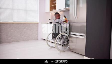 Young Disabled Man Sitting On Wheel Chair Preparing Food In Kitchen Stock Photo