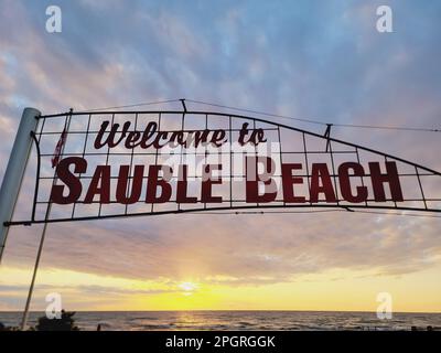 A welcome sign with red letters at the entrance to Sauble Beach with a sunset sky in the background. Stock Photo